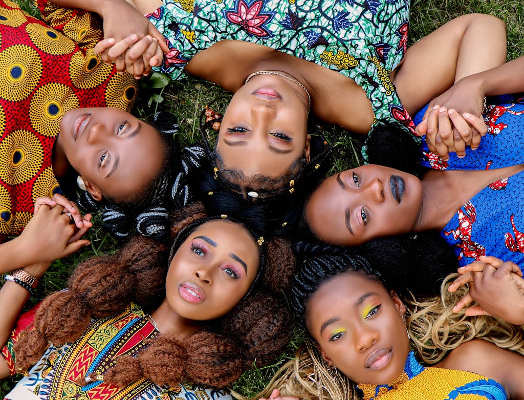 A group of diverse African women lying on grass holding hands, symbolizing unity.