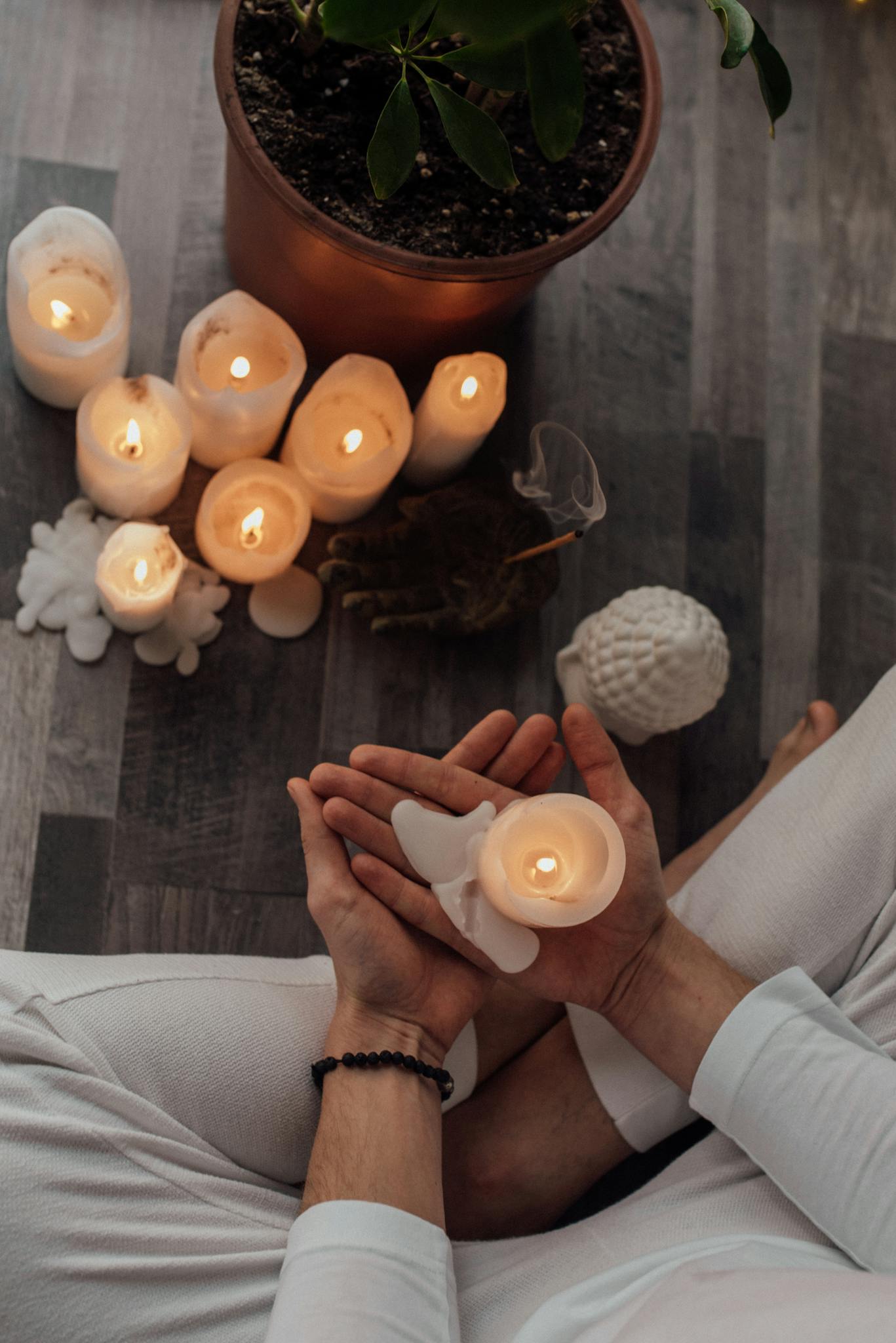 A serene meditation setup with glowing candles and a green potted plant on a wooden floor.