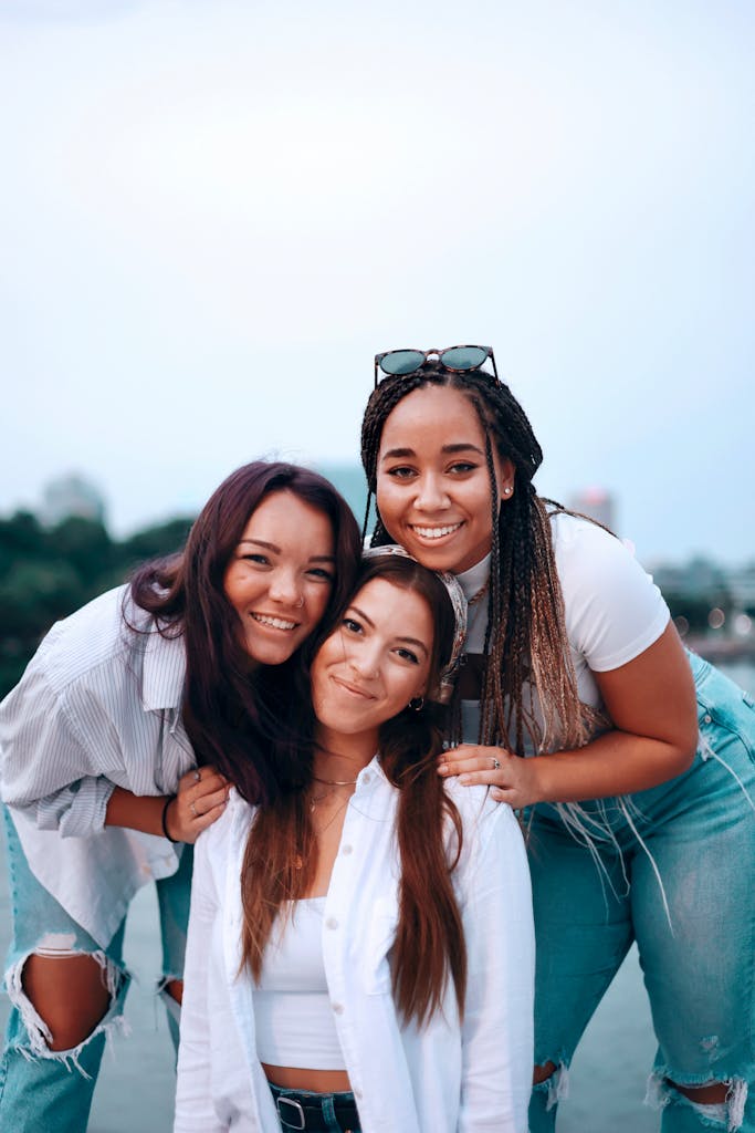 Three diverse young women smiling and posing together outdoors, showcasing friendship.