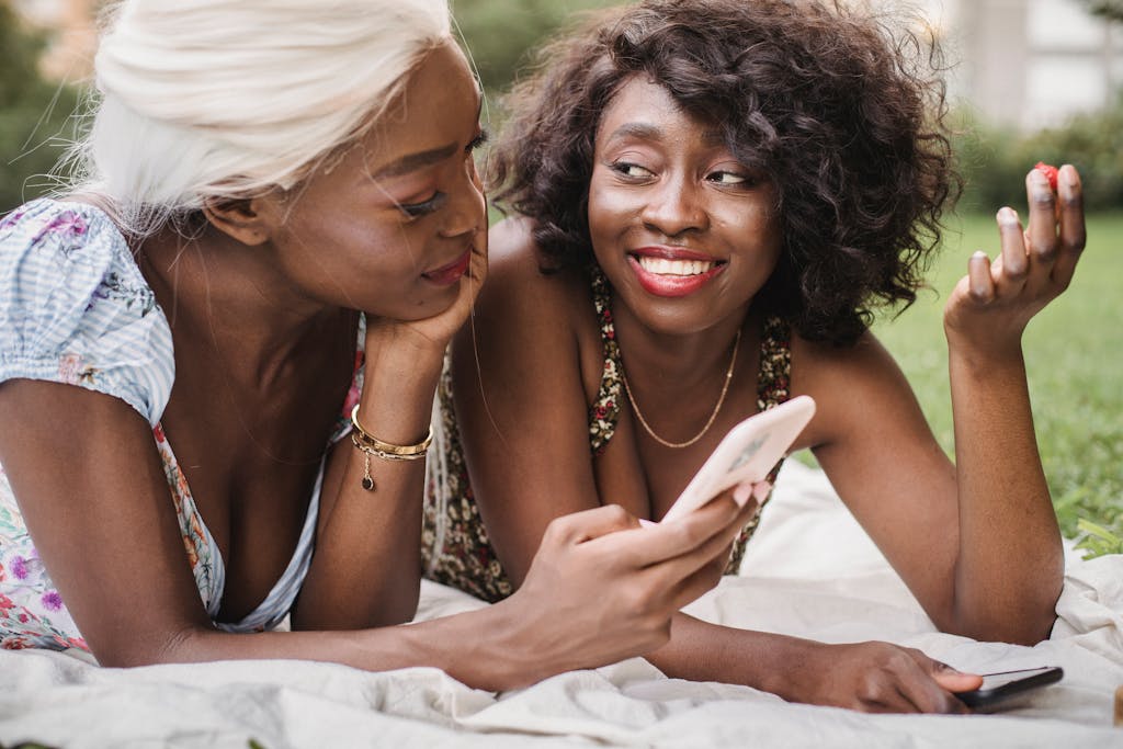Two friends with smartphones enjoying a lively conversation while relaxing outdoors on a sunny day.