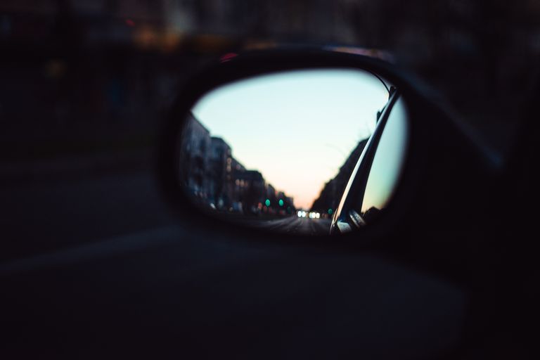 City street scene reflected in car mirror during twilight. Urban life captured in evening light.