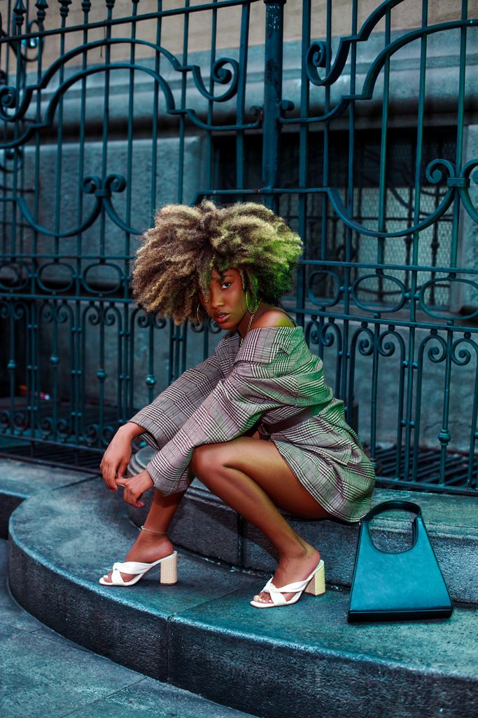 Fashionable woman with afro hair poses in stylish attire on city steps, exuding confidence.